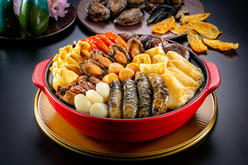traditional asian luxury treasure premium seafood Peng cai abalone, sea cucumber, scallop, prawn, oyster, mushroom in hot clay pot on red table for Chinese new year cuisine halal banquet food menu