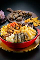traditional asian luxury treasure premium seafood Peng cai abalone, sea cucumber, scallop, prawn, oyster, mushroom in hot clay pot on red table for Chinese new year cuisine halal banquet food menu