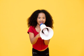 Young mixed race Afro girl talking on megaphone making announcement in yellow color isolated...