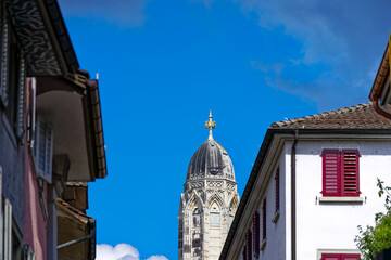 Fototapeta na wymiar Alley at the old town of City of Zürich with church tower of Great Minster church in the background on a sunny summer noon. Photo taken August 5th, 2023, Zurich, Switzerland.