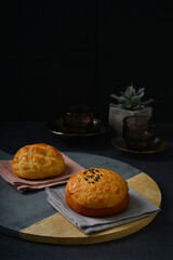 freshly handmade baked Macau crispy round polo bun bread w red bean paste on dark black luxury background with ceramic decoration halal food dessert menu for cafe
