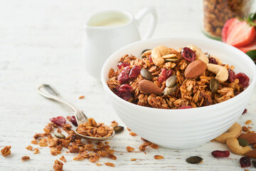 Homemade granola in glass jar with greek yogurt or milk and cashews, almonds, pumpkin with dried cranberry seeds in on white rustic wooden table background. Healthy energy breakfast or snack. Top view