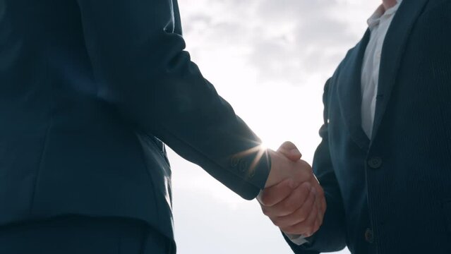 Close-up slow-motion two business partners male female handshaking meet and shake hands, man and woman in formal suits greeting outdoors in city, bright sunlight. sunbeams, sunny day, sun rays