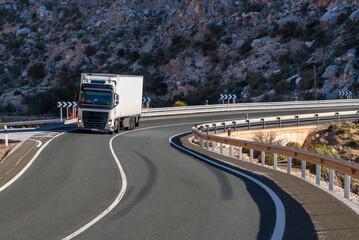 Truck with a refrigerated semi-trailer driving on a winding mountain road