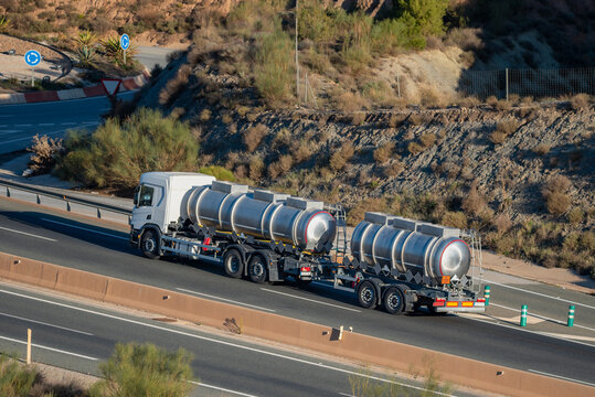 Tanker truck with trailer loaded with dangerous goods, with labels for corrosive liquids, side view.