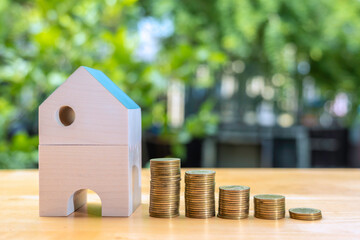 Coins stack near  the wooden home on wooden table to save the money invest for the future. Concept for loan, property ladder, financial, mortgage, real estate investment, taxes and bonus.