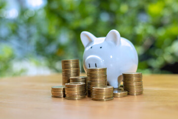 Coins stack in front of white piggy bank on wooden table, Save money concept, Property investment, house loan, reverse mortgage, gold coins money stack growth, saving money coins stack future for home