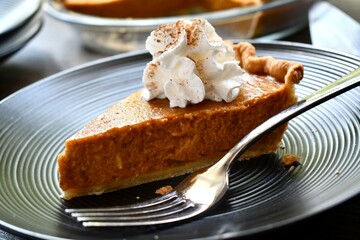 Slice of pumpkin pie with whipped cream on a black plate