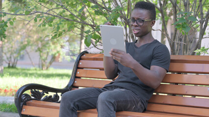 Fototapeta premium Young African Man Upset by Loss on Tablet while Sitting Outdoor on a Bench
