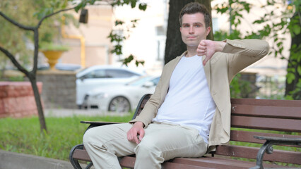 Thumbs Down by Casual Young Man while Sititng Outdoor