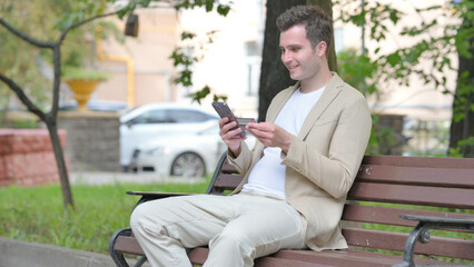 Fototapeta premium Casual Young Man Doing Online Shopping on phone while Sitting Outdoor
