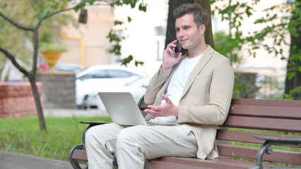 Casual Young Man Talking on Phone and Using Laptop Outdoor