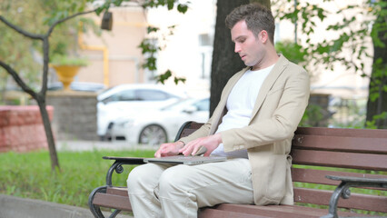 Obraz premium Casual Young Man Coming, Sitting on Bench and Working on Laptop