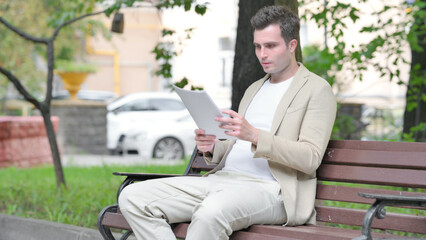 Fototapeta premium Casual Young Man Reading Documents while Sitting Outdoor
