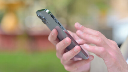 Close Up of Casual Young Man Browsing Smartphone while Sitting Outdoor on a Bench