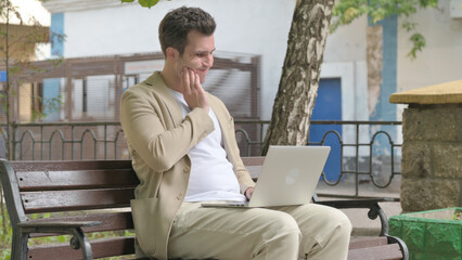 Young Man with Toothache Working on Laptop Outdoor