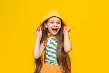 A little girl scout, smiling happily in a summer hat with a backpack. Hiking for children in nature. Yellow isolated bright background.