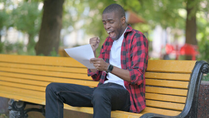 Young African Man Celebrating while Reading Contract Outdoor