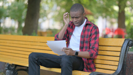 Fototapeta premium Young African Man Feeling Upset while Reading Contract Outdoor