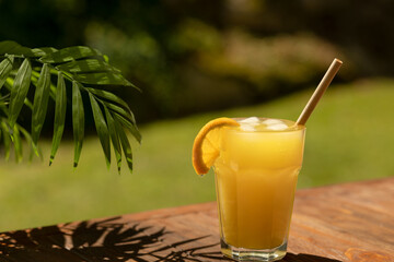 A glass of fresh orange juice on a wooden table under a palm tree branch