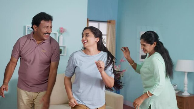 Joyful indian middle aged parents with daughter dancing together at home - concept of Pround parents, Graduation Celebration and Marriage or wedding fix.