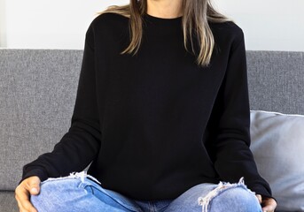 Woman sitting on sofa blank black sweatshirt. Black sweatshirt mockup with copy space. 