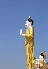 Standing Buddha statue in Thai temple on blue sky background