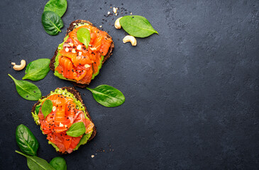 Avocado and salmon sandwich or toast on rye bread with spinach, crushed cashew nuts and sesame...