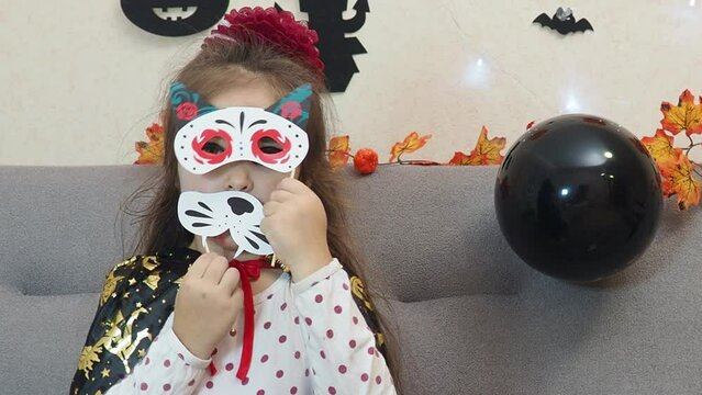 a girl in a vampire costume makes scary faces. cat mask. All Saints' Day. Happy brother and sister on Halloween. Funny kids in carnival costumes indoors. Cheerful children play with pumpkins and candy