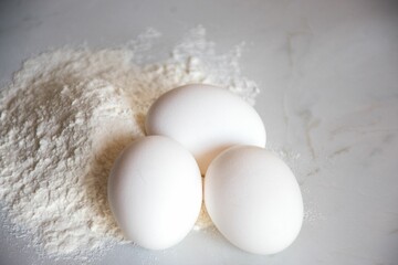 Closeup of a tabletop featuring eggs and flour.