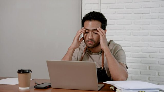 Asian man cafe owner sitting in cafe, man had very serious expression, both hand gripping temples with headache, sternly scrutinizing meager profits shop, was so tired that wanted close business.