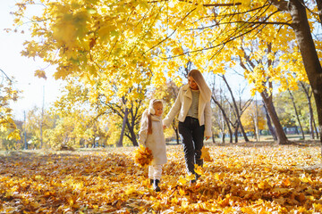 Happy mother and daughter have fun in autumn park at sunset. Stylish mother and daughter enjoy the autumn park. Family on a walk. Childhood, walks, rest.