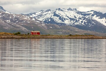 a large lake surrounded by snow-covered mountains, with a bright red house in the frame