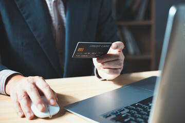 businessman uses a computer laptop and credit card to buy or purchase produce payment online and sits on the chair in the living room at home. The concept of finance and online shopping.