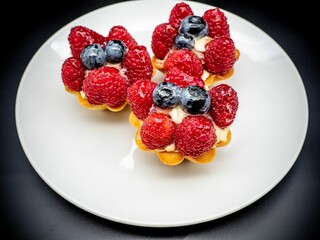 Closeup of three mini tarts with sweet cream and fresh berries on the round white plate