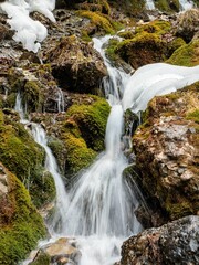 Scenic view of a small waterfall cascading down over a rocky mountain range, surrounded by snow