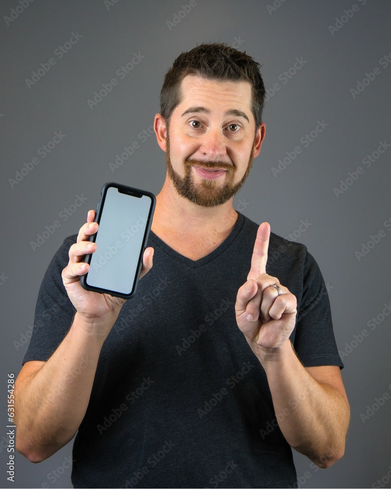 Wall mural joyful young man holding and pointing at a modern smartphone in his hand, with copy space