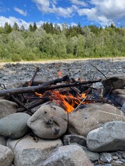 small camp fire in riverbed with forest and blue sky