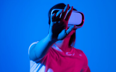 Female gamer entering a game while wearing virtual reality goggles in neon light. Young woman experiencing immersive technology in a studio.