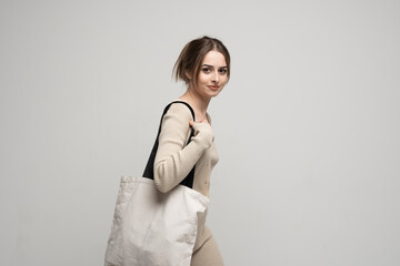 Cheerful happy woman in a beige costume with white cotton bag in her hands. Mockup and zero waste concept. Eco friendly lifestyle. Reuse, recylce, zero waste, No more plastic.