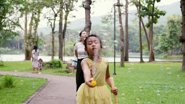 Little girl having fun playing soap bubbles while walking with mother in tha park.