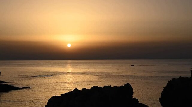 Sonnenuntergang an felsiger K&uuml;ste mit vorbeifahrenden Booten