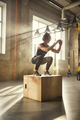 Challenging myself. Side view of athletic woman in sportswear doing squat while standing on wooden box at gym