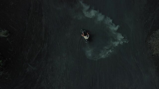 A young man drifts on a motorcycle on black volcanic lava, top view. Drift on volcanic sand, clouds of sand rise. Spectacular stunts on a motorcycle in the sand.