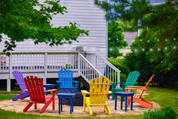 set of colorful wooden adirondack chairs around fire pit in the garden on the backyard - 631572635