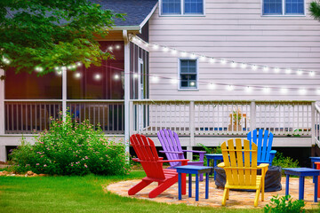 set of colorful wooden adirondack chairs around fire pit in the garden on the backyard