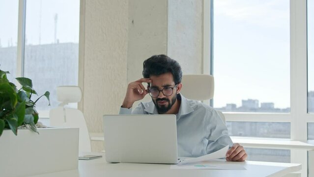 Stressful overwhelmed Arabian Indian man anxious businessman work on laptop check documents business commerce upset office manager accountant analyzing paper contract financial mistake debt problem