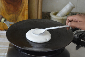 spreading batter for making dosa on an iron pan, a south Indian food. Fermented Indian food.