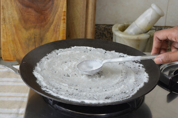 spreading batter for making dosa on an iron pan, a south Indian food. Fermented Indian food.