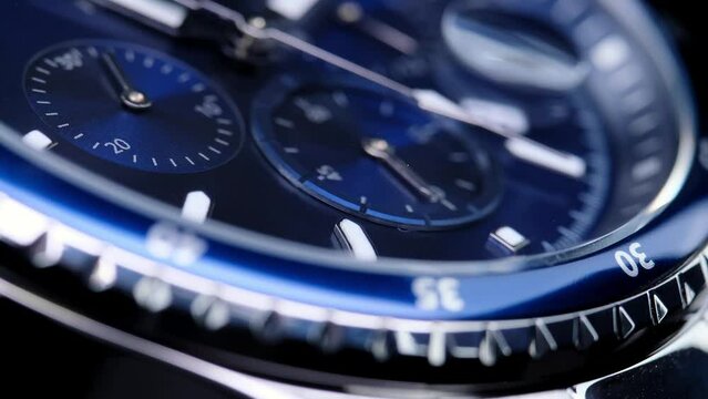 second hand ticking on a blue watch face. Men's chronograph watch in metal with sapphire crystal. closeup view of rotating watch, running second arrow. blue dial